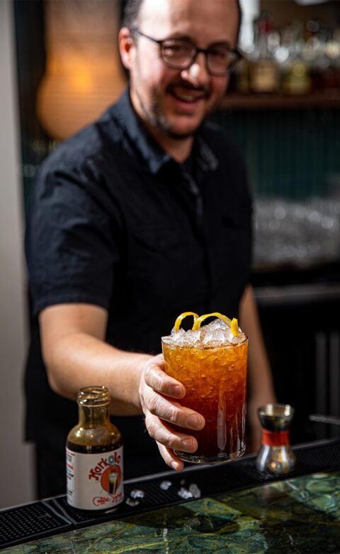 man in black shirt serving a black iced tea garnished with a lemon twist