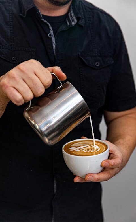 man in black shirt making a latte with latte art