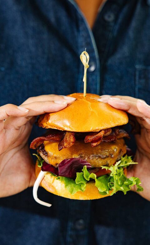 a person holding a bacon cheeseburger in their hands