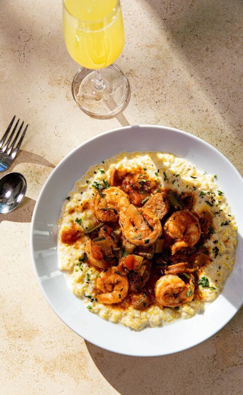 a plate of shrimp and grits with a glass of orange juice