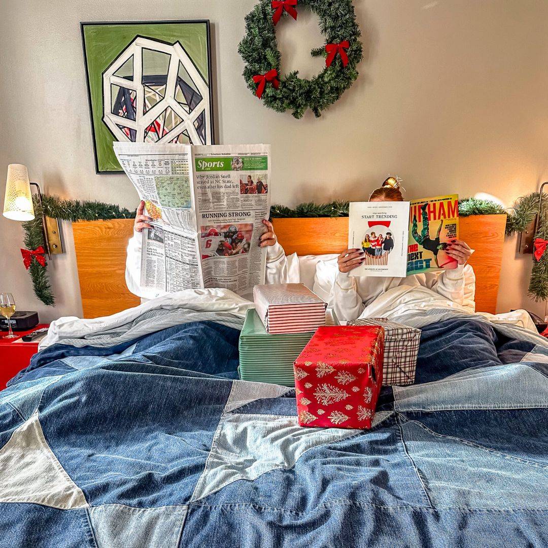 a couple reading newspapers in bed covered with christmas presents